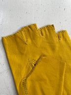 Close-up view of a pair of yellow, deadstock Ines Vintage - Fingerless Fashion Leather Driving Gloves made by Ines Gloves, laying on a white surface. The stitching details are visible, especially around the finger openings and the reinforcement areas on the gloves. The surface underneath is slightly weathered.