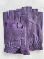 Close-up of a pair of Ines Vintage - Fingerless Fashion Leather Driving Gloves from Ines Gloves, showcased on a white surface. The stylish purple gloves feature decorative stitching and multiple oval perforations along the back for ventilation. An adjustable strap with a Velcro closure is visible on one glove, ensuring a secure fit.