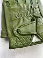Close-up of a pair of Ines Vintage - Fingerless Fashion Leather Driving Gloves by Ines Gloves in green leather with intricate stitching. The gloves feature an overlapping strap with a snap button closure. The stitching along the edges forms a diamond pattern, while the main body has zigzag stitches. Small holes are visible near the knuckles.