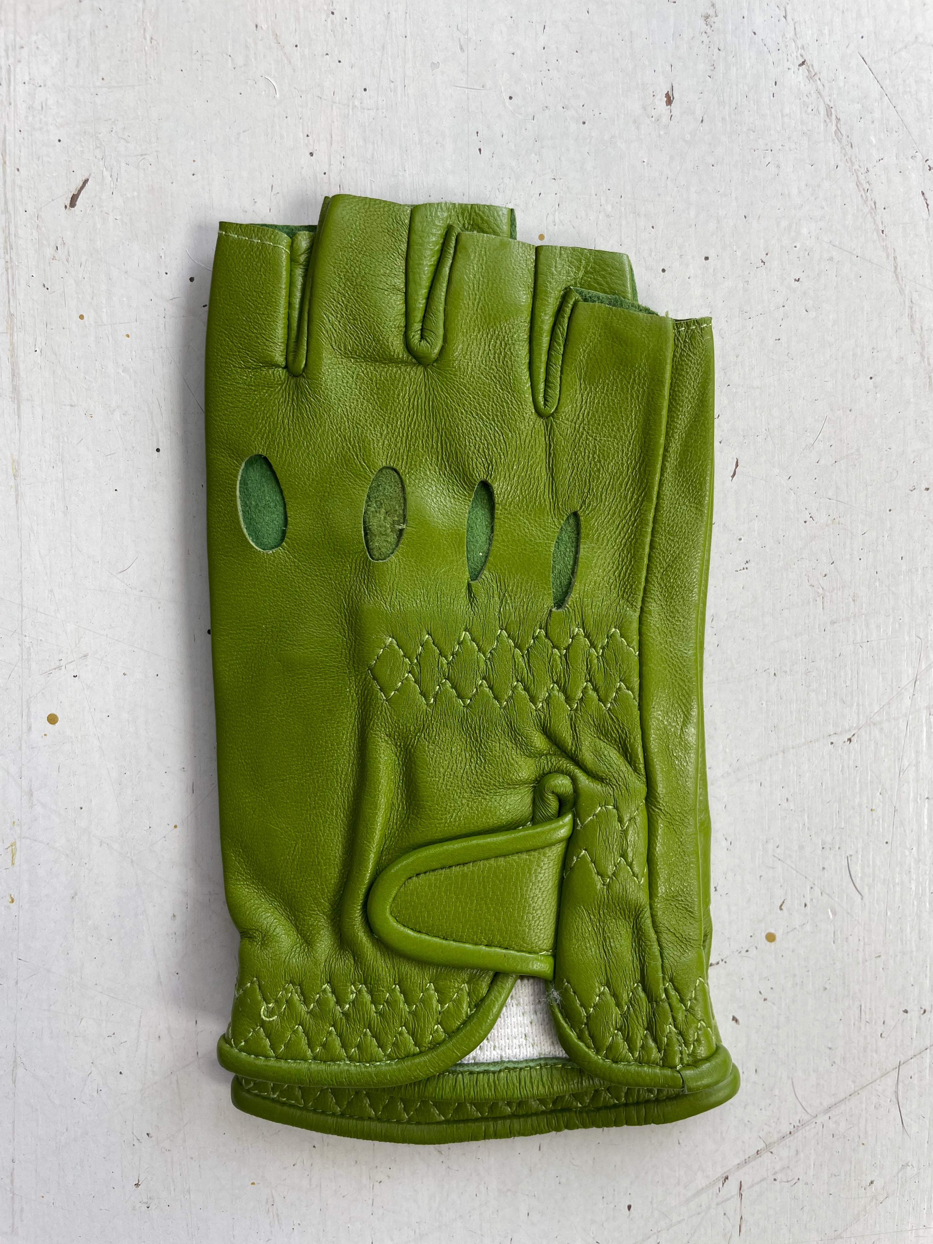 An Ines Vintage fingerless fashion leather driving glove from Ines Gloves lies flat on a light-colored surface. This fashionable glove features three oval cutouts on the back and detailed stitching around the wrist area. A Velcro strap for securing the glove is visible, partially overlapping the stitched section.