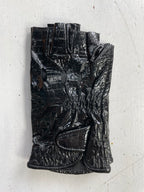 A single Ines Vintage - Fingerless Fashion Leather Driving Glove in black is laid flat on a textured white surface. This glove, part of the Ines Gloves collection, features small cutouts around the knuckles and a Velcro strap at the wrist. The crocodile-embossed leather is shiny and crinkled, giving it a worn appearance.
