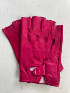 A pair of **Ines Vintage - Fingerless Fashion Leather Driving Gloves** by **Ines Gloves** in a fashionable, bright pink color on a white surface. These gloves feature three oval-shaped ventilation holes on the back of each hand and a zigzag stitching pattern. They have an adjustable strap with a Velcro closure near the wrist for a secure fit.