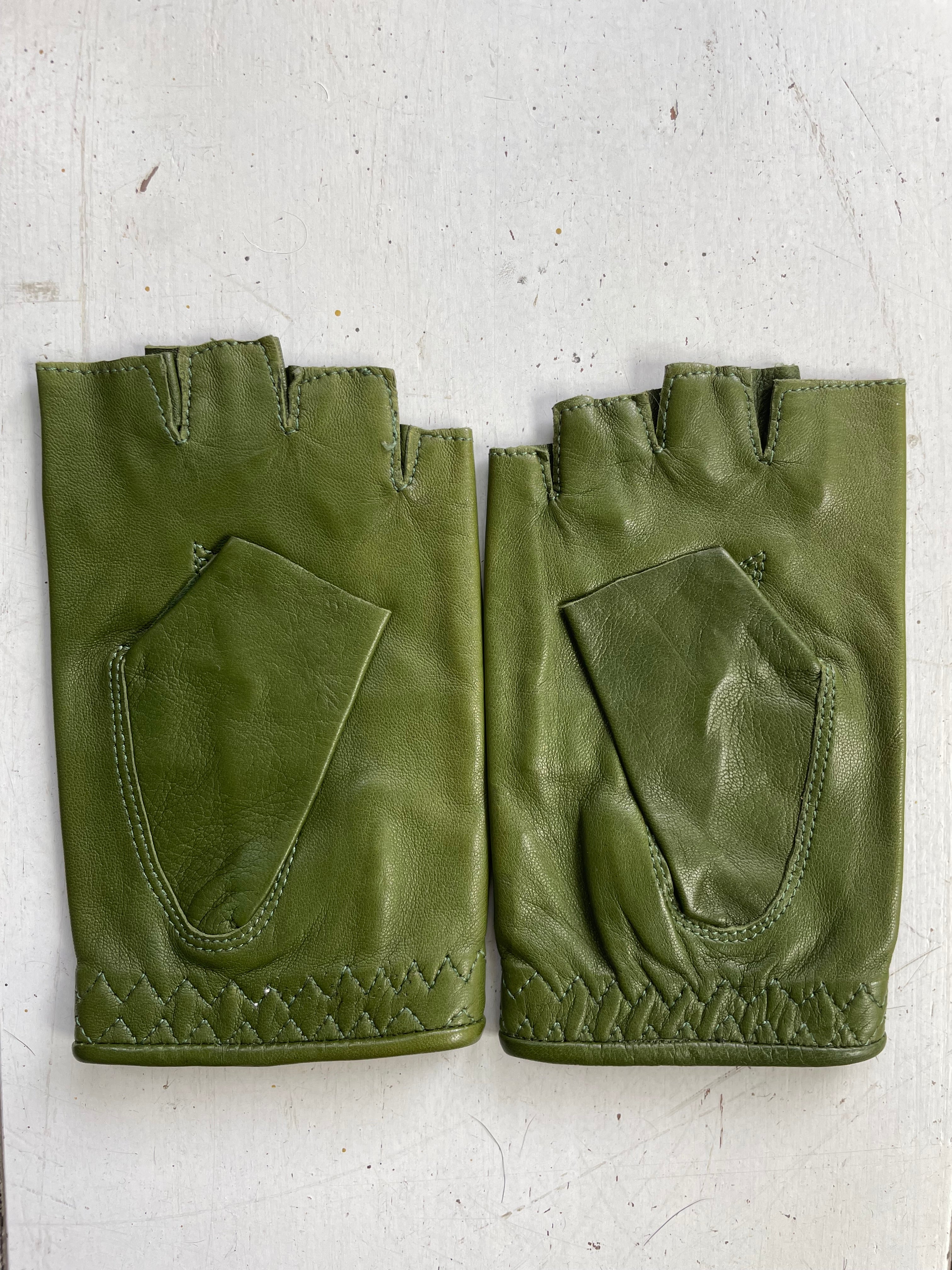 The "Ines Vintage - Fingerless Fashion Leather Driving Gloves" by Ines Gloves are displayed on a white surface. This pair of stylish green leather gloves features quilted stitching along the bottom edge and extra padding on the palms. Both gloves have small openings for the fingers and appear to be in excellent condition.