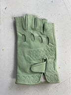 The Ines Vintage - Fingerless Fashion Leather Driving Glove by Ines Gloves lies on a white textured surface. This fashionable light green glove features three oval ventilation holes on the back, intricate stitching in a pattern near the wrist, and a Velcro strap closure at the base for adjustment. The leather material appears soft and slightly worn.