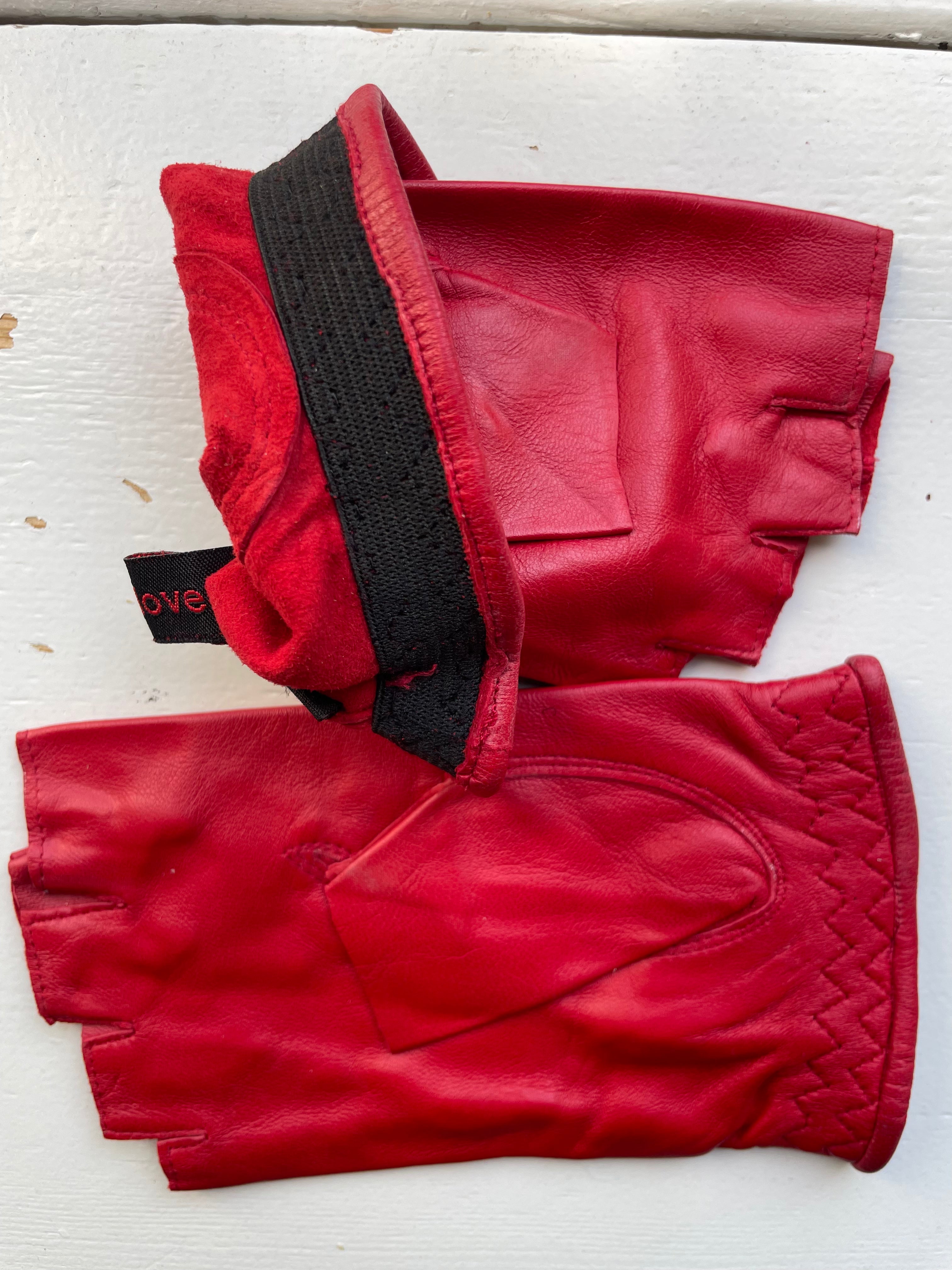 The Ines Vintage - Fingerless Fashion Leather Driving Gloves by Ines Gloves are displayed side by side on a light-colored surface. The stylish red gloves feature a black adjustable strap across the wrist, padding on the palm, and visible stitching, especially around the thumb area of the right glove.