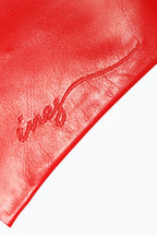 Close-up of a red leather surface with the words "Classic long opera leather gloves" stitched in cursive script. The stitching, also red, blends subtly with the leather, adding a delicate textural contrast reminiscent of elegant evening gloves from Ines Gloves. The smooth, polished leather gives a rich and vibrant look against a plain white background.
