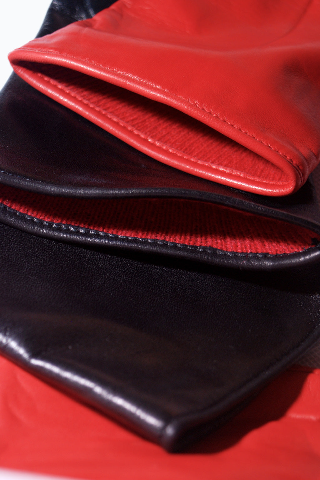 Close-up of neatly stacked red and black Long cashmere lined gloves by Ines Gloves, alternating in color. The red gloves have a smooth and shiny texture, while the black gloves appear slightly matte. Each pair boasts a luxurious cashmere lining, enhancing the contrast between colors and highlighting the sleek material.