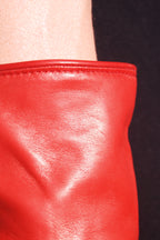 Close-up of a pair of Ines Gloves long cashmere lined gloves, likely a sleeve or long glove, against a dark background. The texture of the leather is smooth with visible creases and a shiny finish. The top edge of the garment has a neatly stitched seam, and a beige area, possibly a person's arm, is visible at the top.