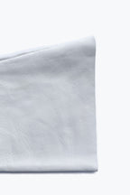 A close-up image of a folded piece of light grey leather. The texture is smooth with subtle fine lines and creases, showcasing natural variations in the material. The edge is neatly stitched, indicating craftsmanship reminiscent of Short fingerless leather fashion gloves by Ines Gloves. The background is plain white.